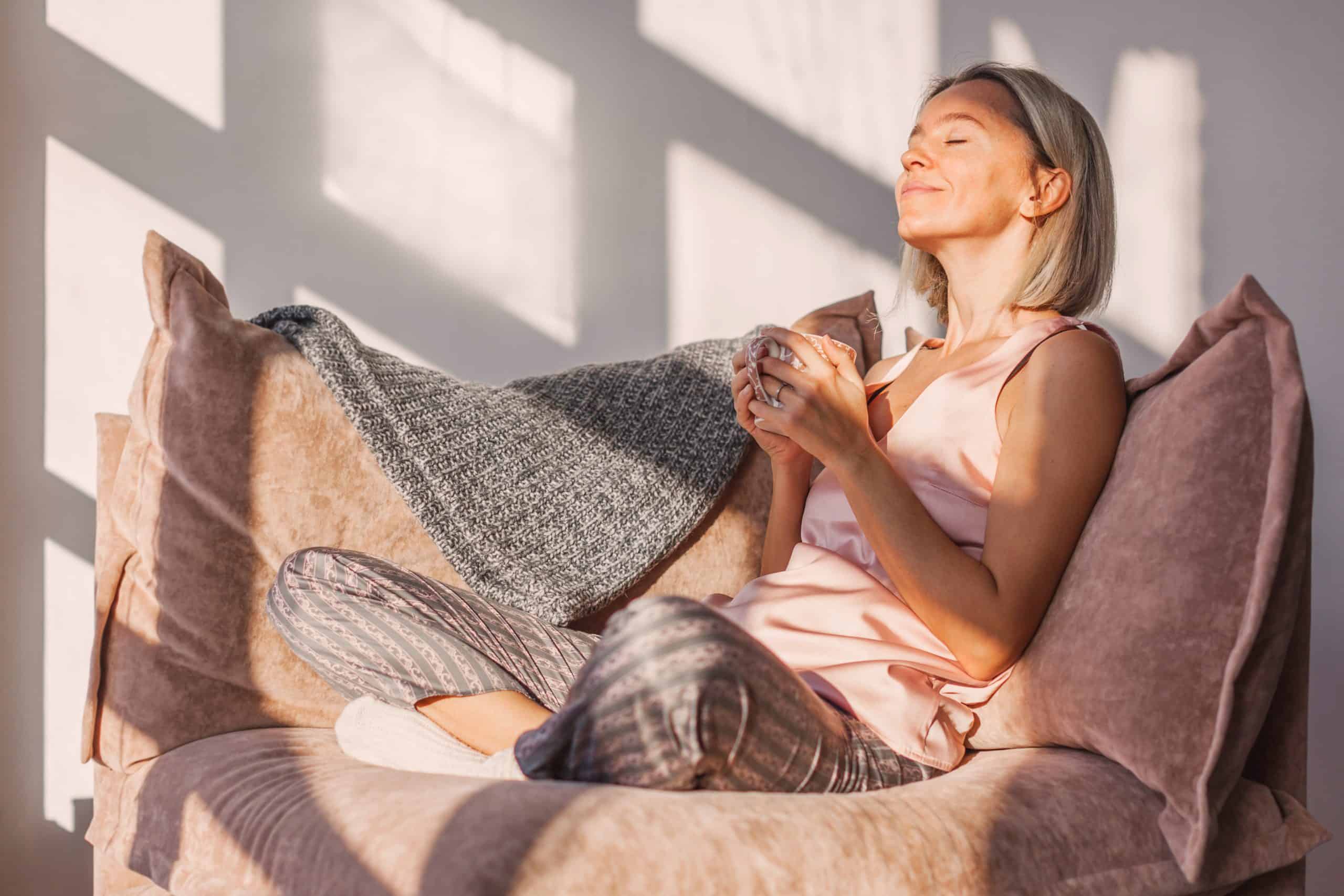 Happy dreamy middle aged woman sitting on sofa in living room wi